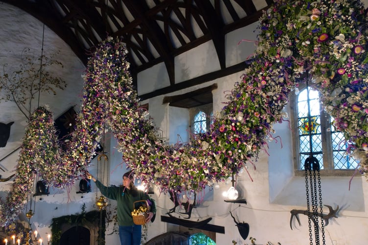 One of the garden team adding the last of the flowers to the 2024 Garland in the Great Hall at Cotehele. ©National Trust Images Steve Haywood.